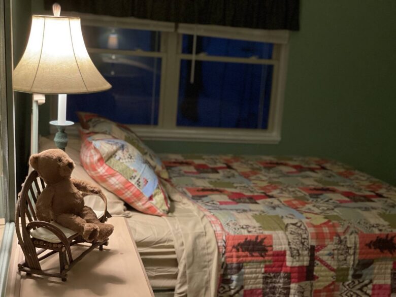 A bed with a patchwork quilt and a teddy bear in a small rocking chair