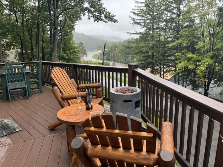 The deck in daylight: log Adirondack chairs around the gas fire table