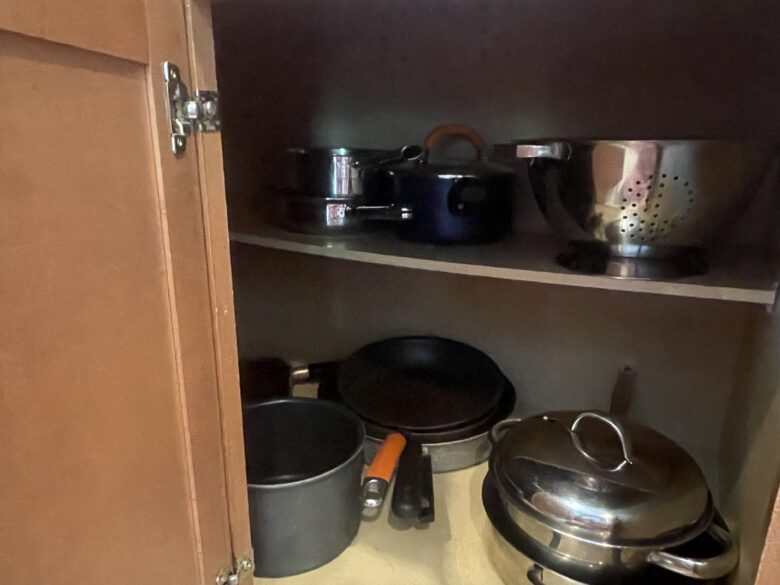 A kitchen cabinet of pots, pans and a colander